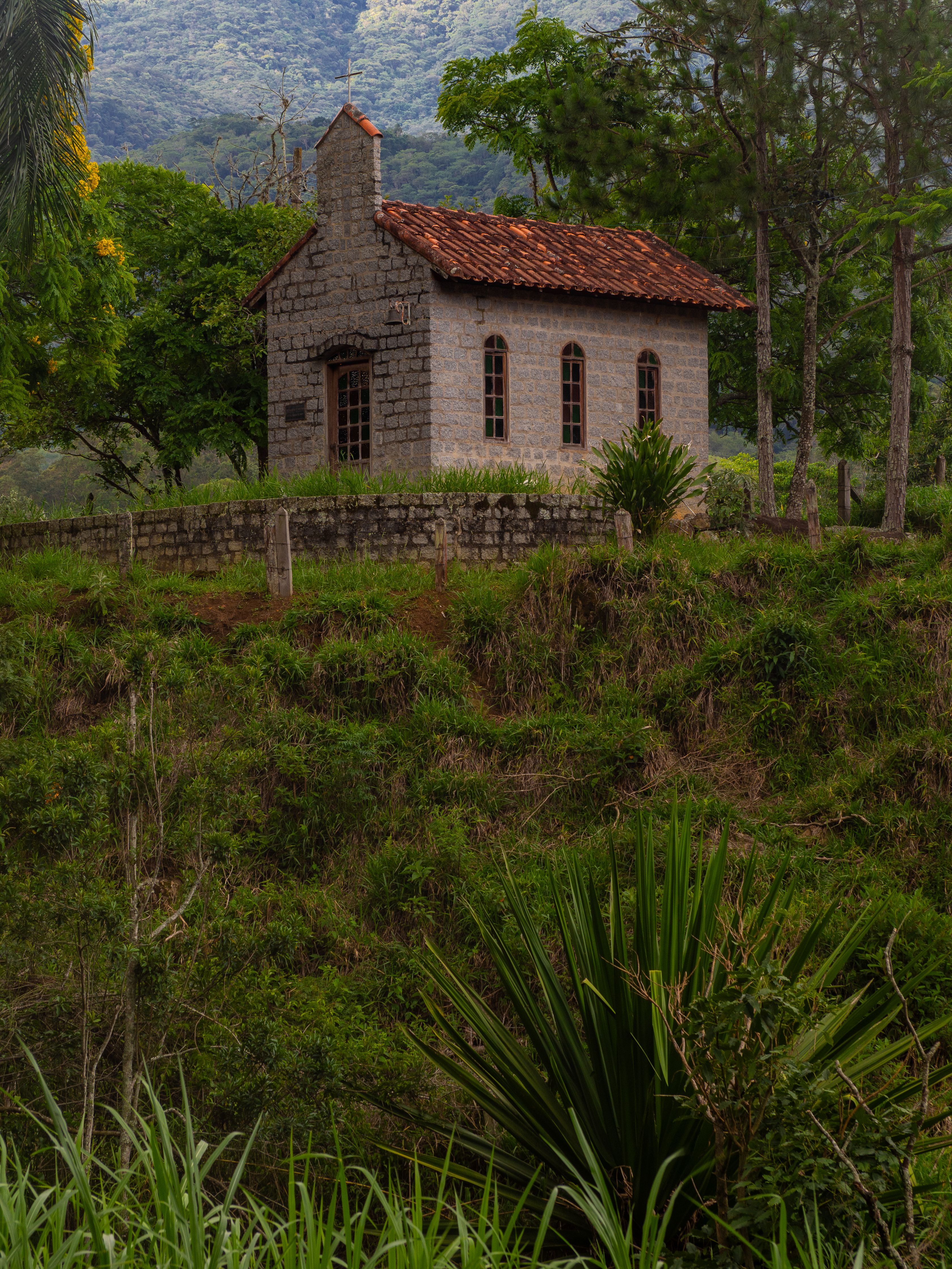 Fotomural Serena capilla de piedra ubicada en un campo verde, rodeada de árboles y hierba.
