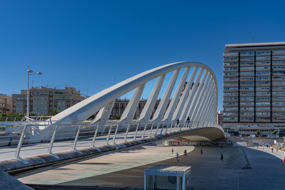 Contemporary white bridge in Valencia, Spain, with urban backdrop and vibrant blue sky.