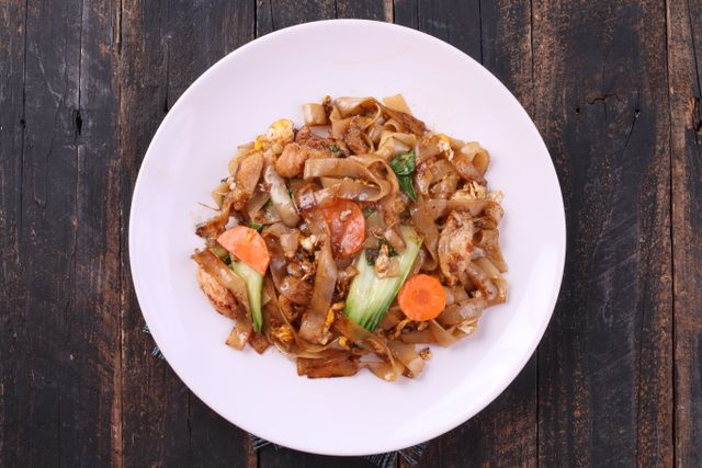 Delicious stir-fried noodles with vegetables served on a white plate over rustic wooden table.