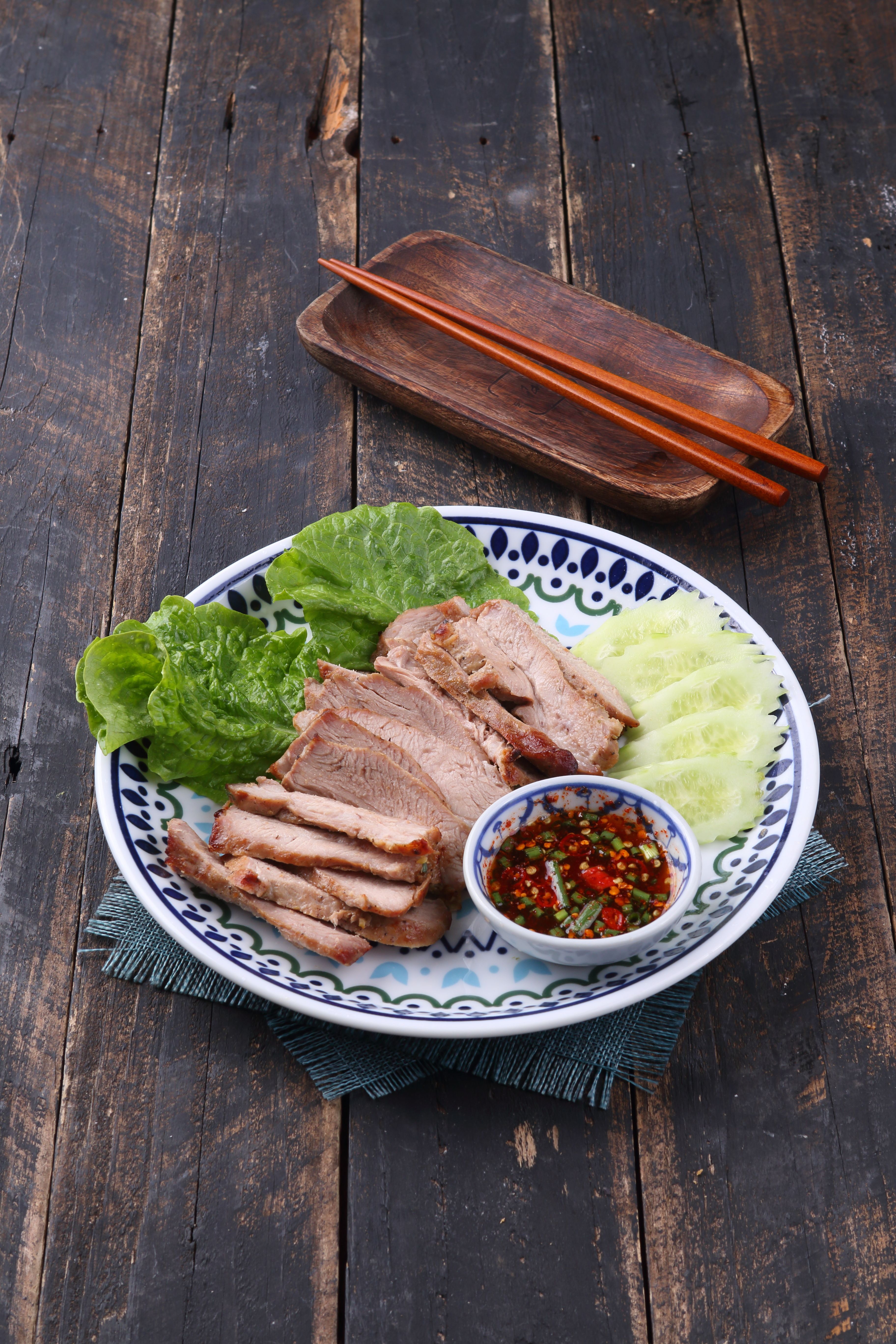 Grilled meat with fresh lettuce and spicy sauce on rustic wooden table.
