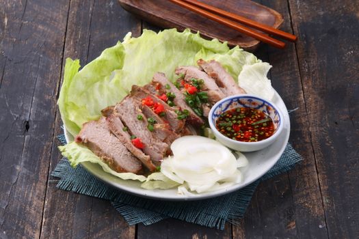 Sliced grilled pork on lettuce with a bowl of spicy dipping sauce.