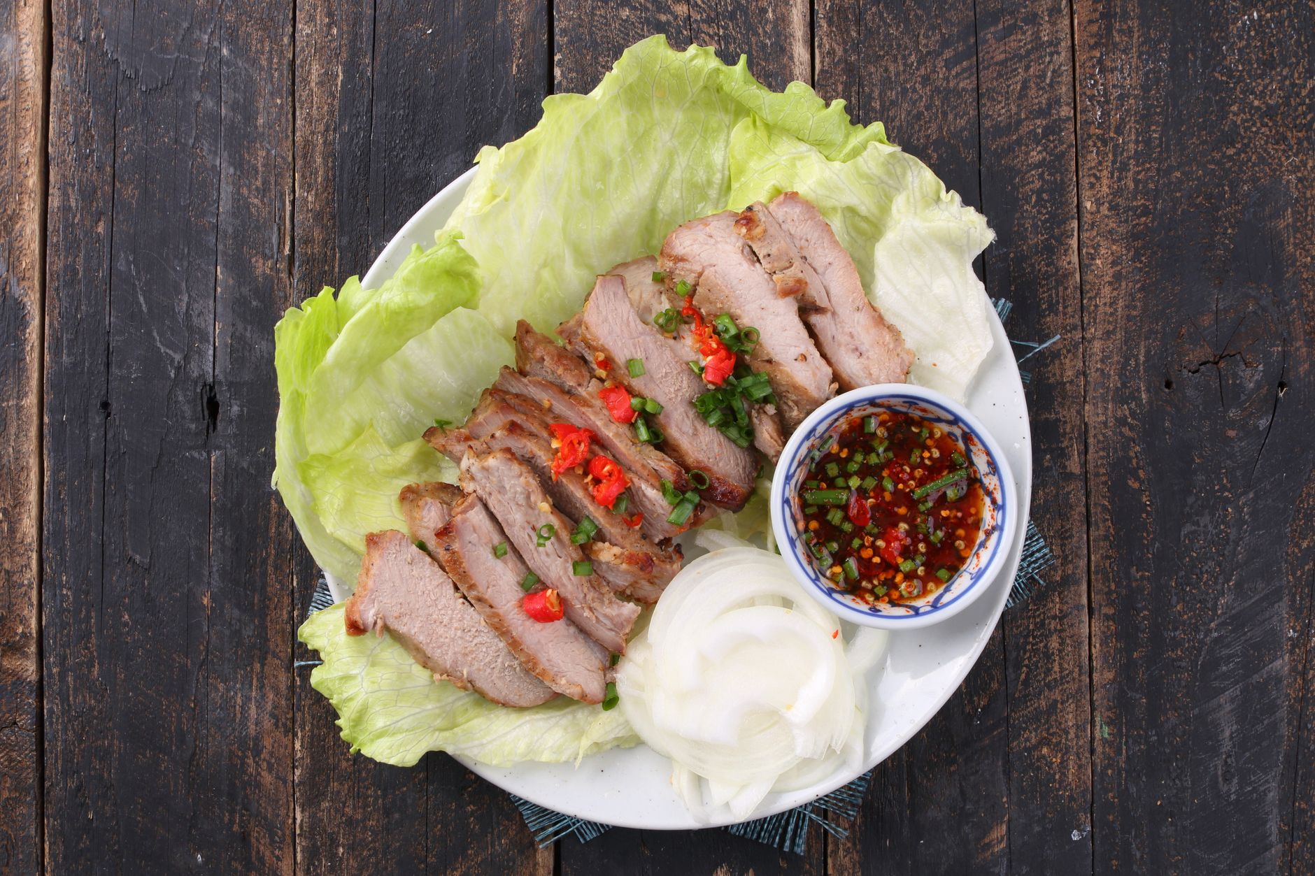 Bowl of Thai grilled pork larb with fresh herbs and lettuce leaves, showing charred meat pieces tossed with bright green cilantro and mint
