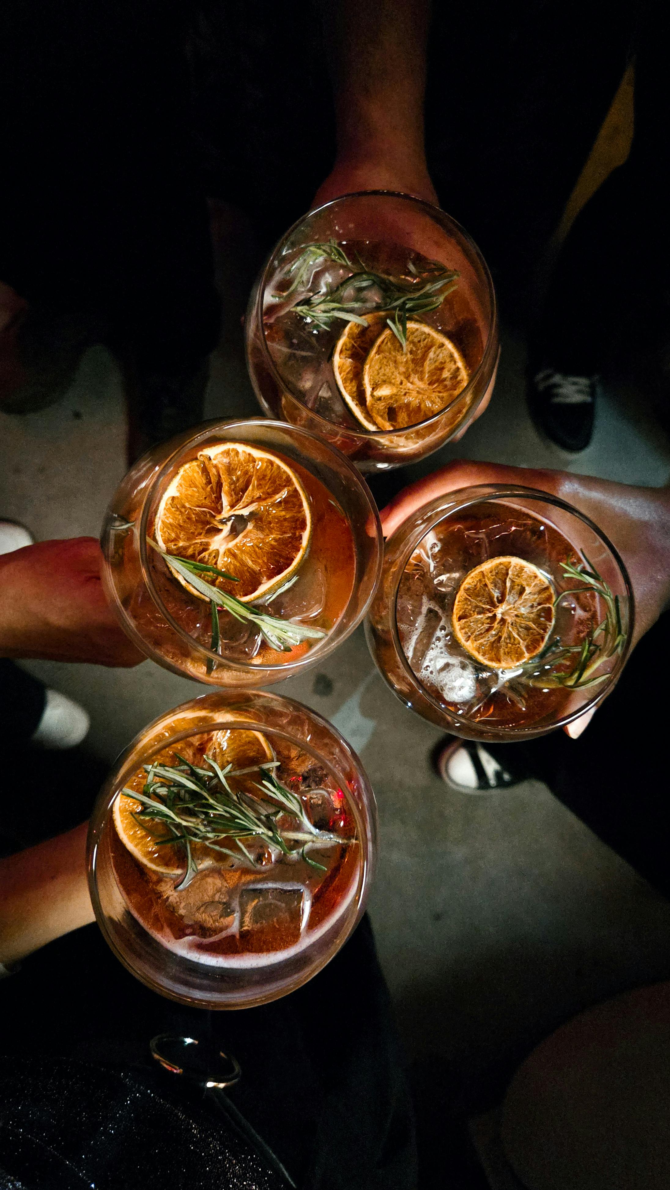 Overhead view of four cocktail glasses with herbs and citrus, capturing a celebratory toast moment.