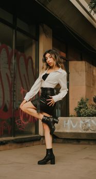 Stylish woman in a chic urban outfit poses confidently against a graffiti wall.
