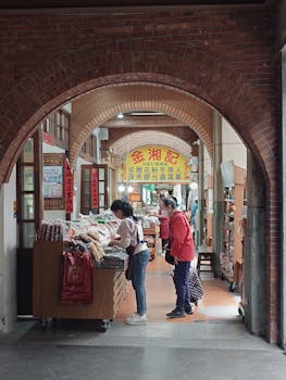 Women browse goods at an indoor traditional market, framed by a brick archway.