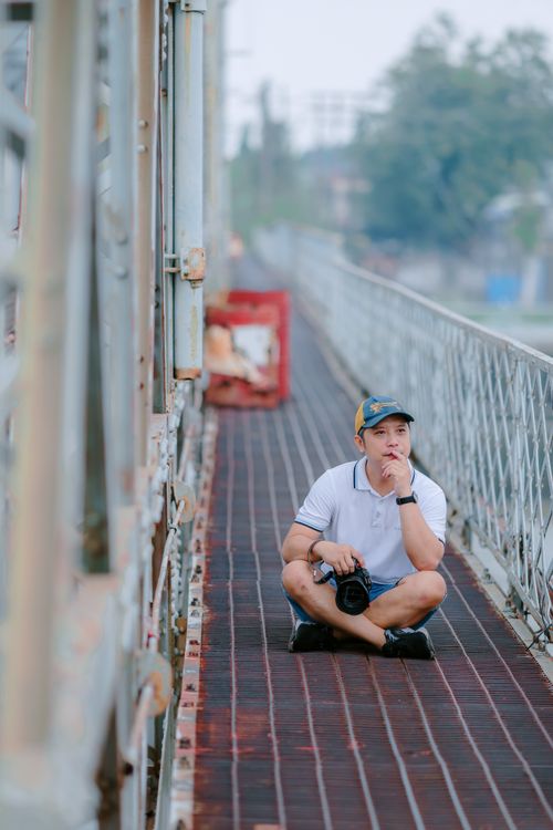 Free Pensive man with camera sitting on an industrial bridge, pondering. Stock Photo