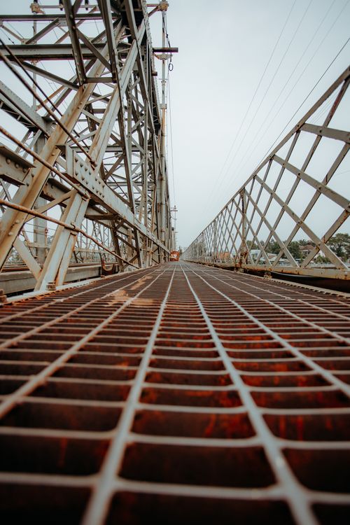 Free Industrial metal bridge with rusty grid perspective against cloudy sky. Stock Photo