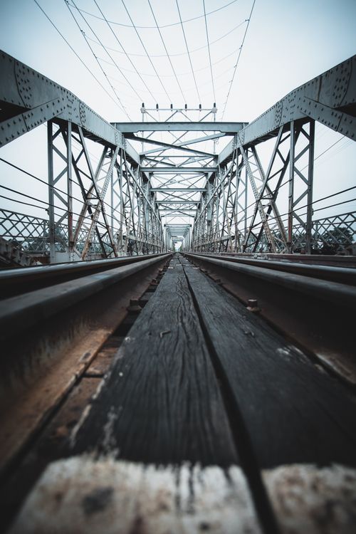 Free Low-angle view of a steel railway bridge on a cloudy day, emphasizing industrial design. Stock Photo