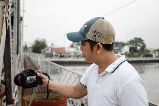 A photographer wearing a cap takes pictures on a historic bridge over a river.