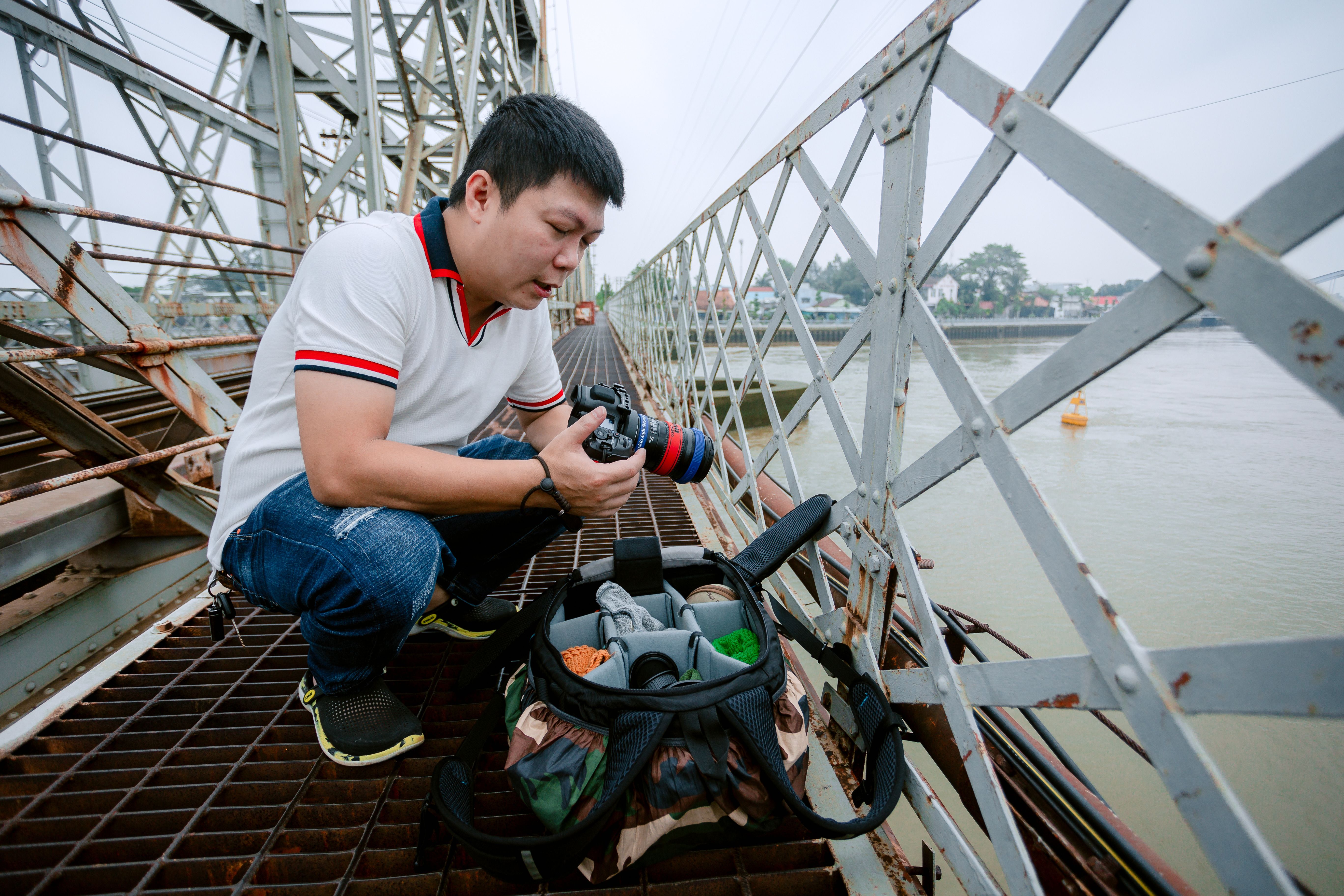 Photographer Examining Camera on Industrial Bridge · Free Stock Photo