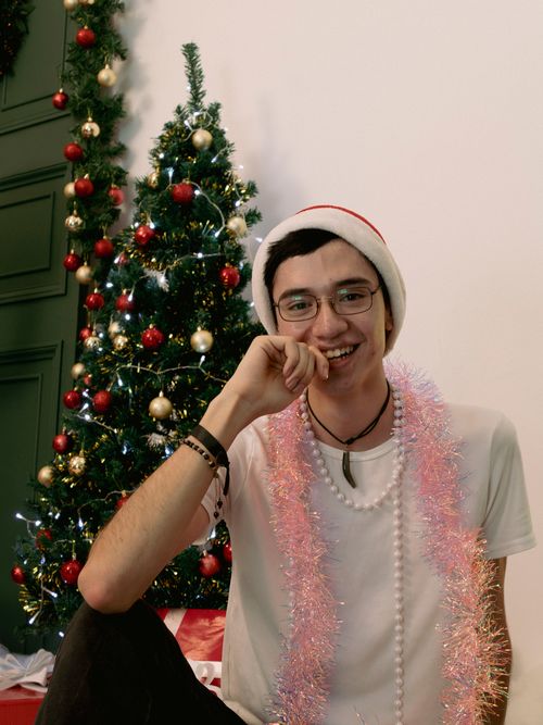 Free Smiling young man in Santa hat by a decorated Christmas tree at home. Stock Photo