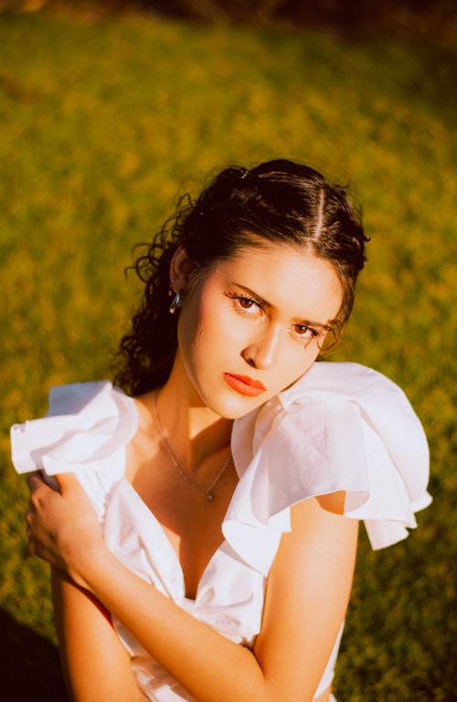 Free A confident young woman in a white dress poses outdoors in warm sunlight. Stock Photo