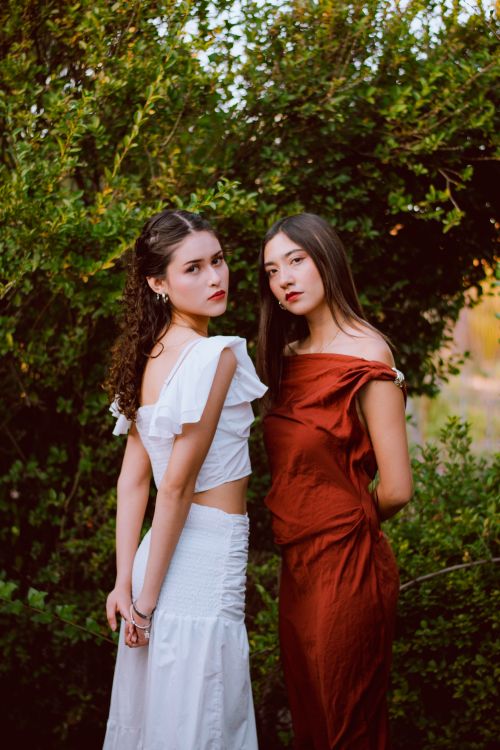 Free Elegant portrait of two women in stylish dresses in a lush outdoor setting. Stock Photo