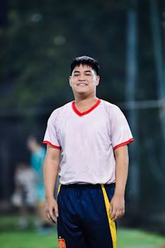 Smiling young man in soccer uniform on an outdoor field in Hanoi at night.