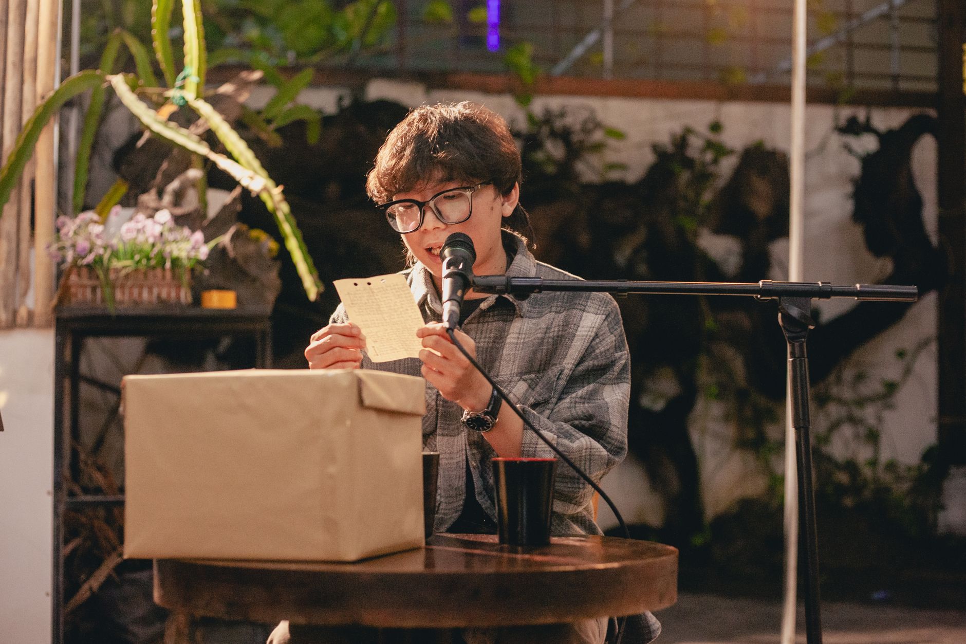 A young man reading a note into a microphone outdoors with a relaxed ambiance.