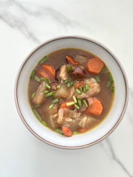 A delicious bowl of vegetable soup with fresh herbs on a white marble surface.
