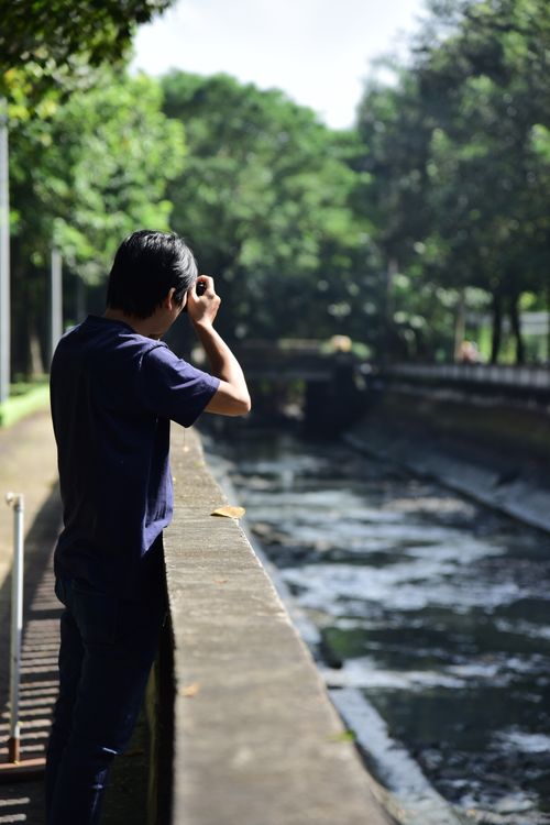 Free A man in casual clothing stands on a bridge looking at a river with lush green trees. Stock Photo
