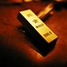 A close-up of a gleaming, inscribed physical gold bar illuminated by warm light.