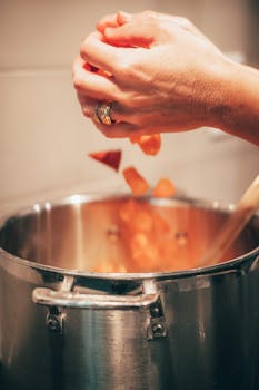 Hands adding diced sweet potatoes into a pot on the stove for cooking.