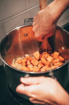 Hands stirring sweet potatoes in a pot, showcasing home cooking.