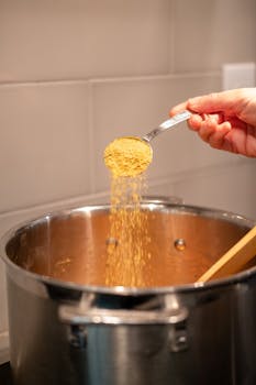 A hand sprinkles seasoning into a pot, enhancing the meal's flavor. Perfect for culinary themes.