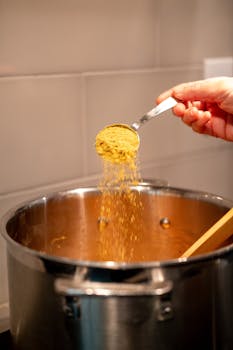 A hand adding curry powder to a cooking pot, enhancing flavors.