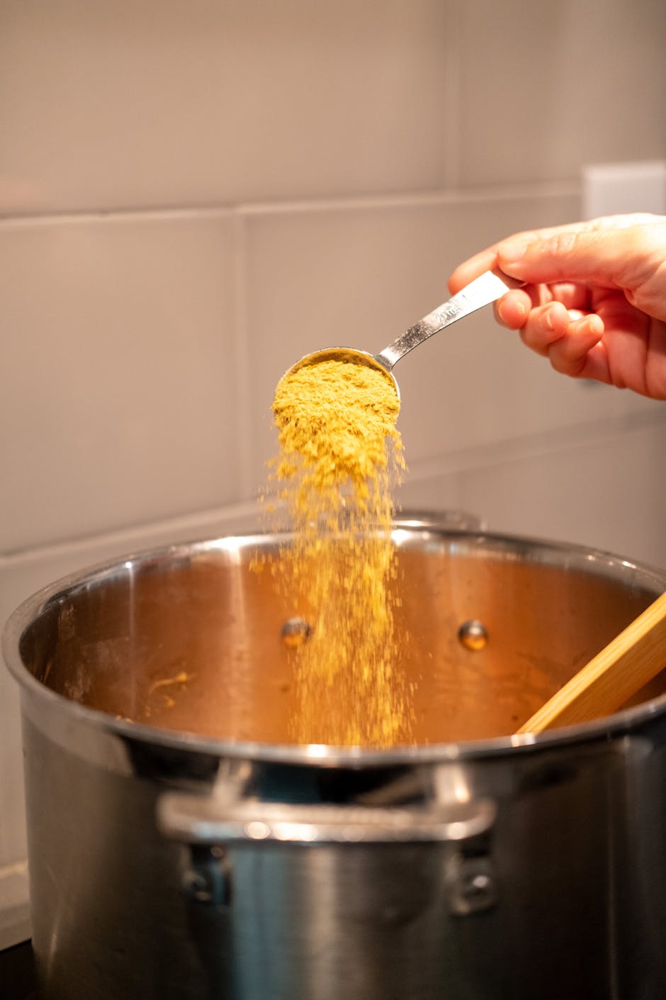 A hand pours spice into a large pot, enhancing a meal. Warm and cozy kitchen scene.