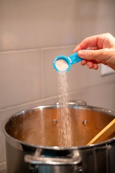 Hand adding salt to a pot for flavorful cooking in a modern kitchen.