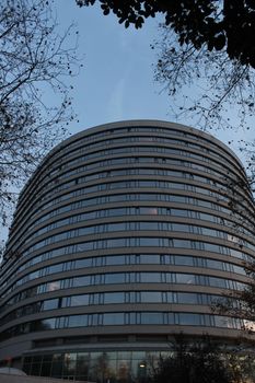 Stunning view of a modern curved building with glass facade surrounded by tree branches.