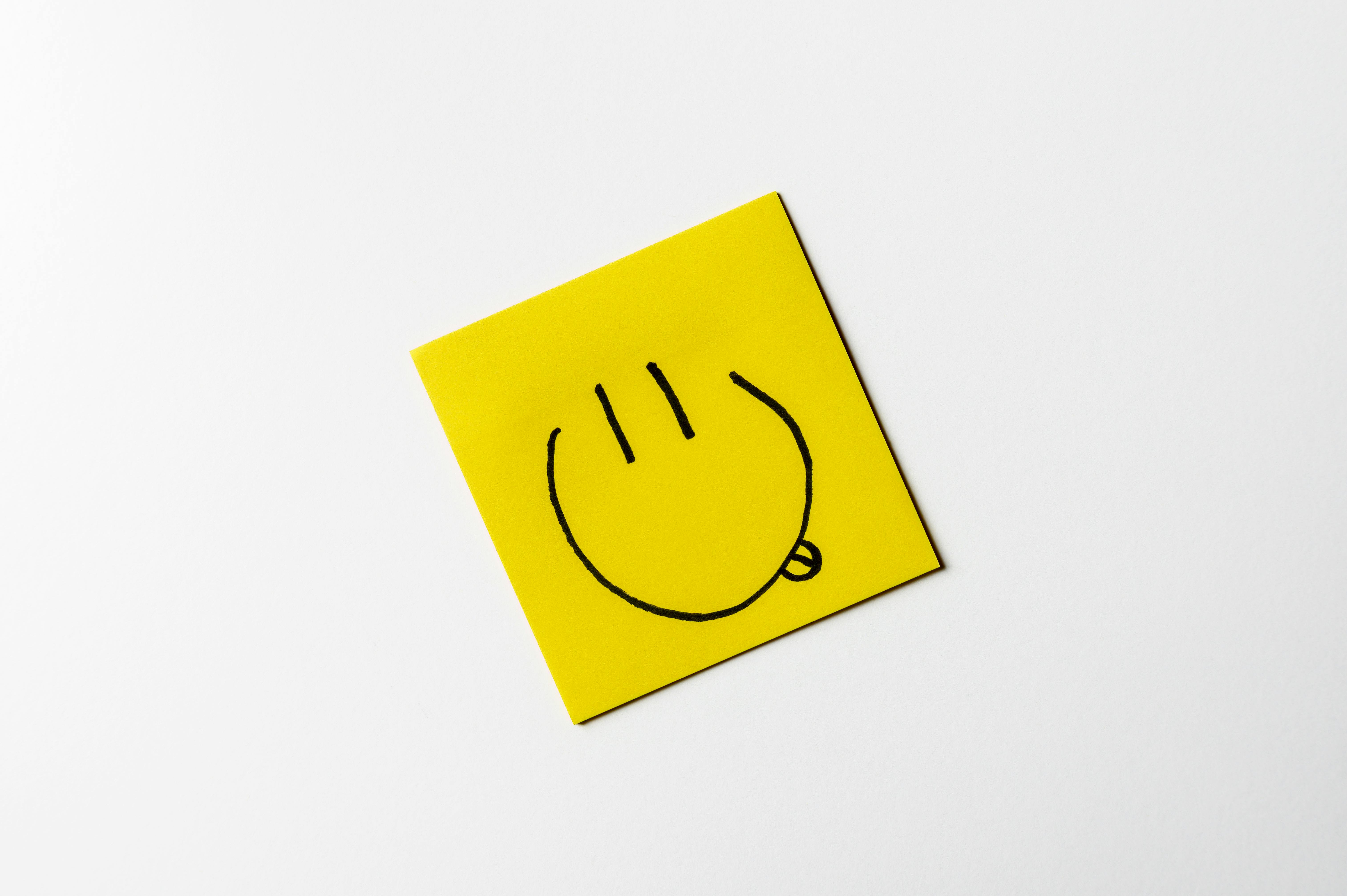 무료 흰색 배경에 노란색 스티커 메모에 그려진 간단한 손으로 그린 웃는 얼굴. 스톡 사진