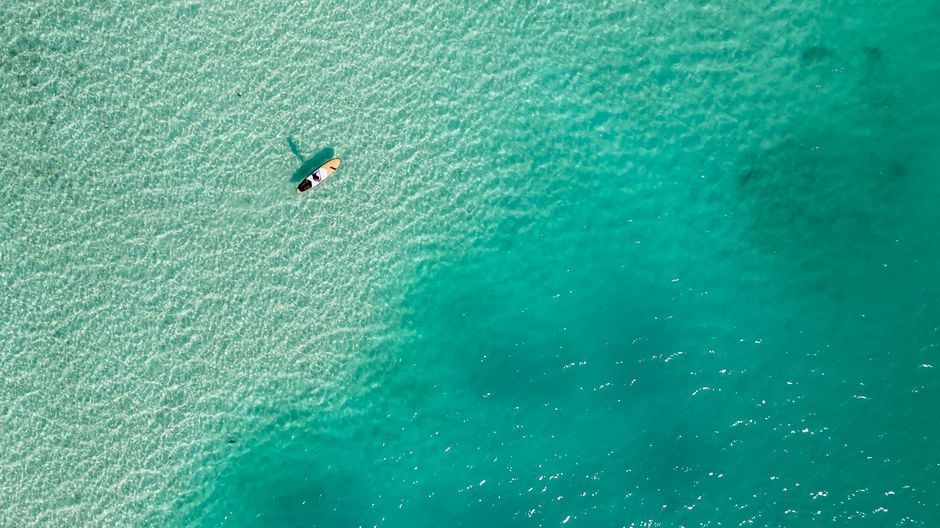 Aerial photograph of a solo paddleboarder navigating turquoise waters, capturing a serene oceanic landscape. - Pebbles Beach Barbados: Racehorses, Paddleboarding, and Food