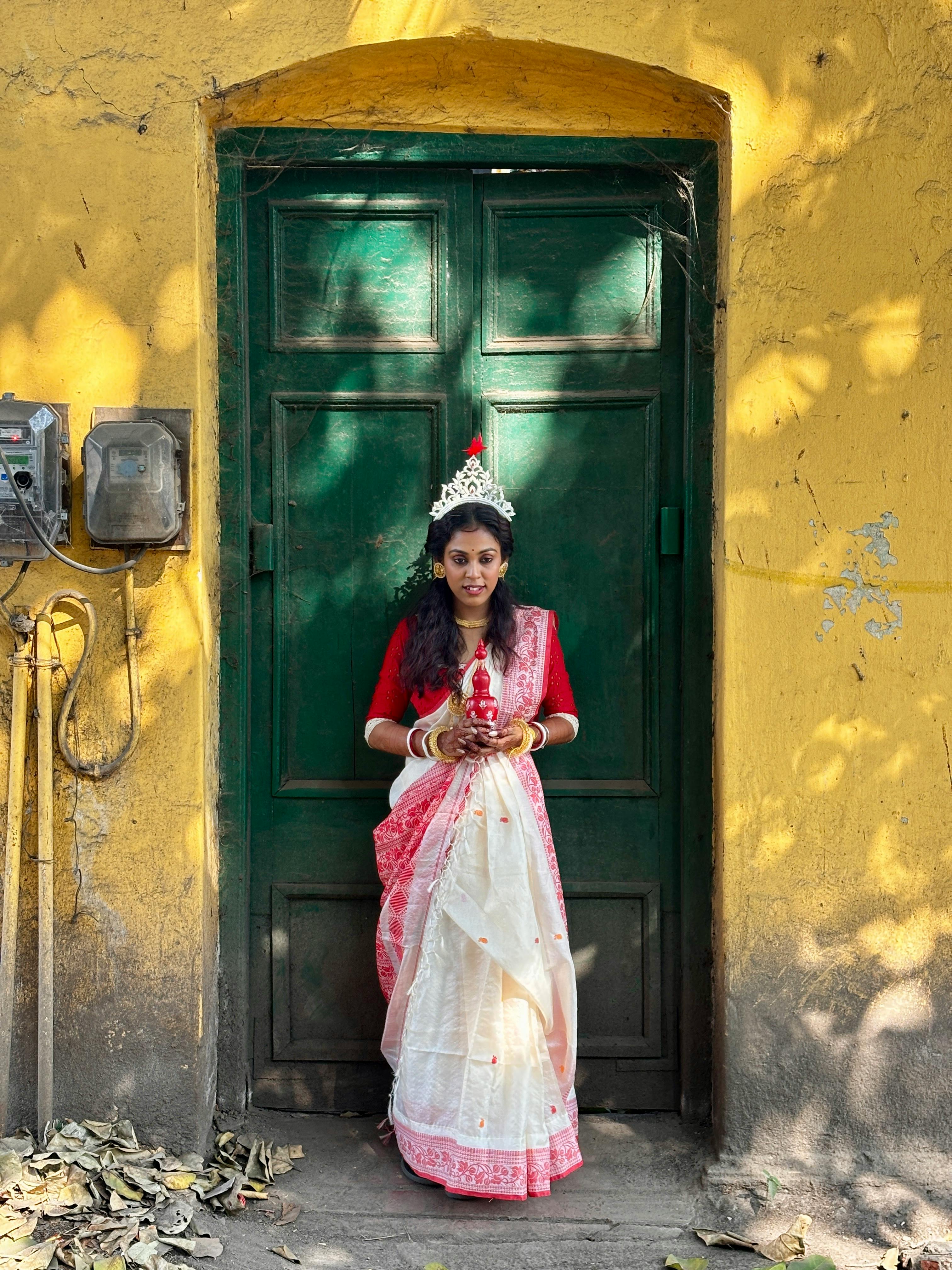 A beautiful South Asian bride in traditional attire poses outdoors in Chinsurah, India.