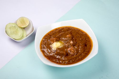 Free Rich Indian butter chicken curry with cucumber and lime sides in bright setting. Stock Photo
