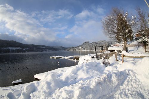Free Serene winter scene of a snow-covered lakeside dock with mountains. Stock Photo