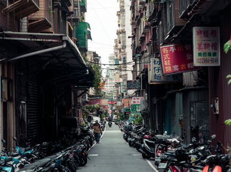 A vibrant street in New Taipei City, Taiwan, lined with scooters and bustling with activity.