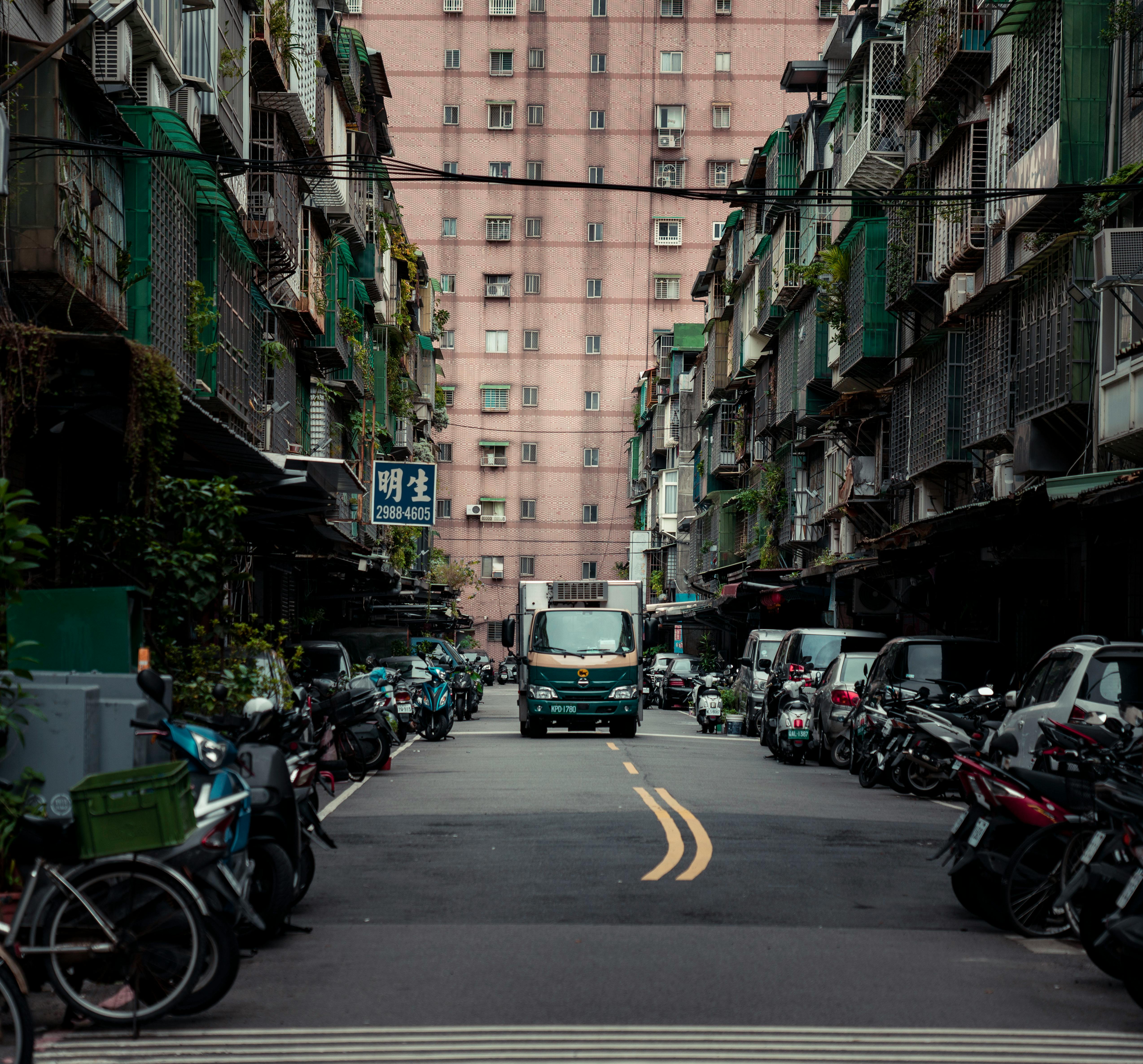 Busy urban street scene in New Taipei City, Taiwan, featuring parked scooters and a delivery truck.