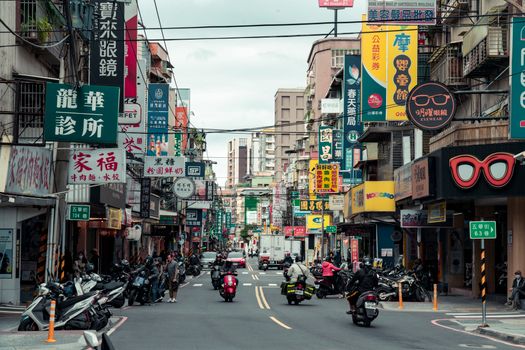Vibrant urban street in New Taipei City, Taiwan, bustling with people, scooters, and colorful signs.