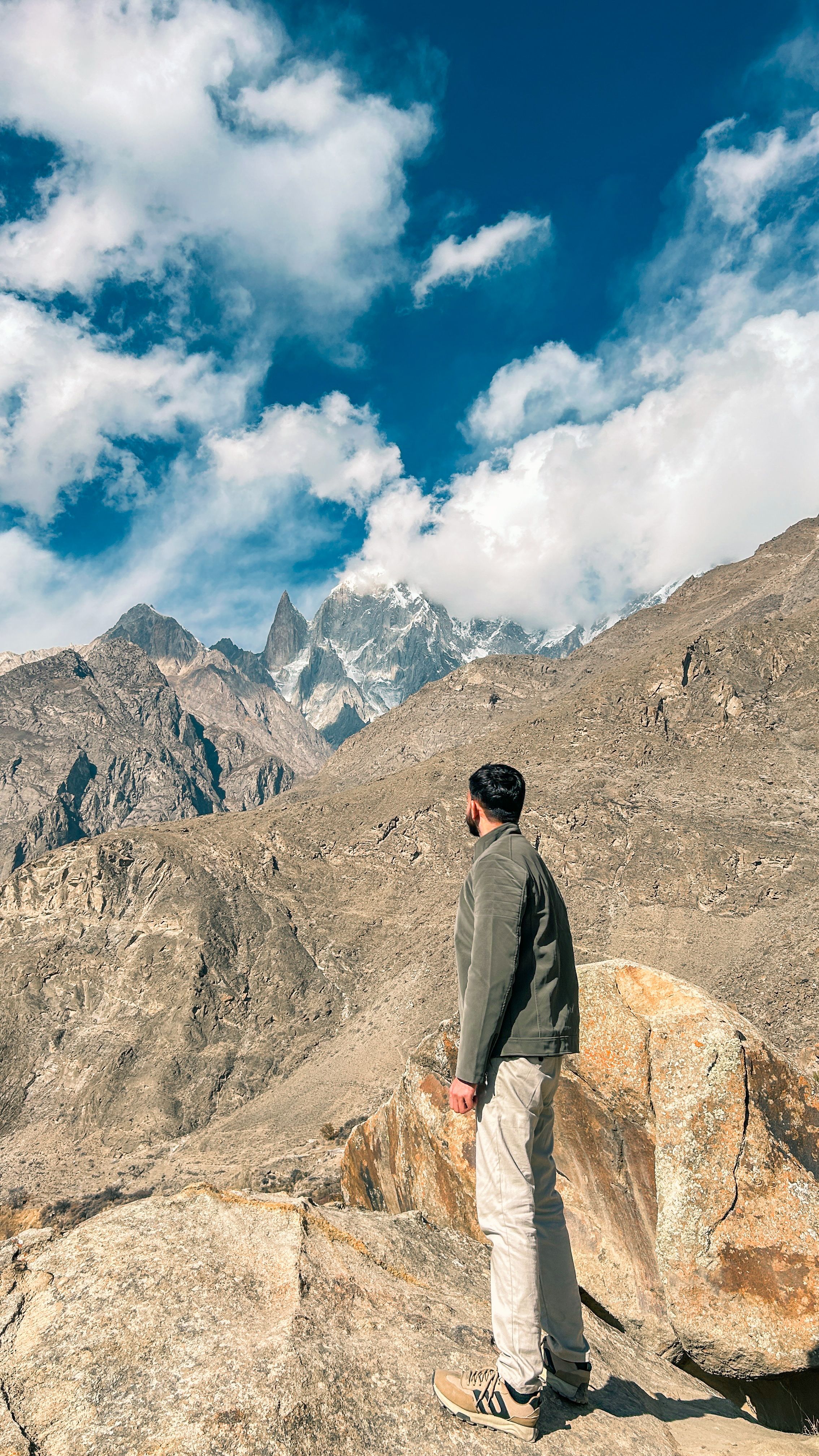 A man stands on a rock, admiring the stunning mountain views in Hunza Valley, Pakistan.