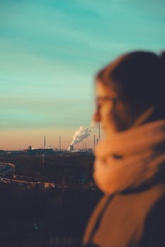 A silhouette of a person at sunset overlooking a factory emitting white smoke in Duisburg, Germany.