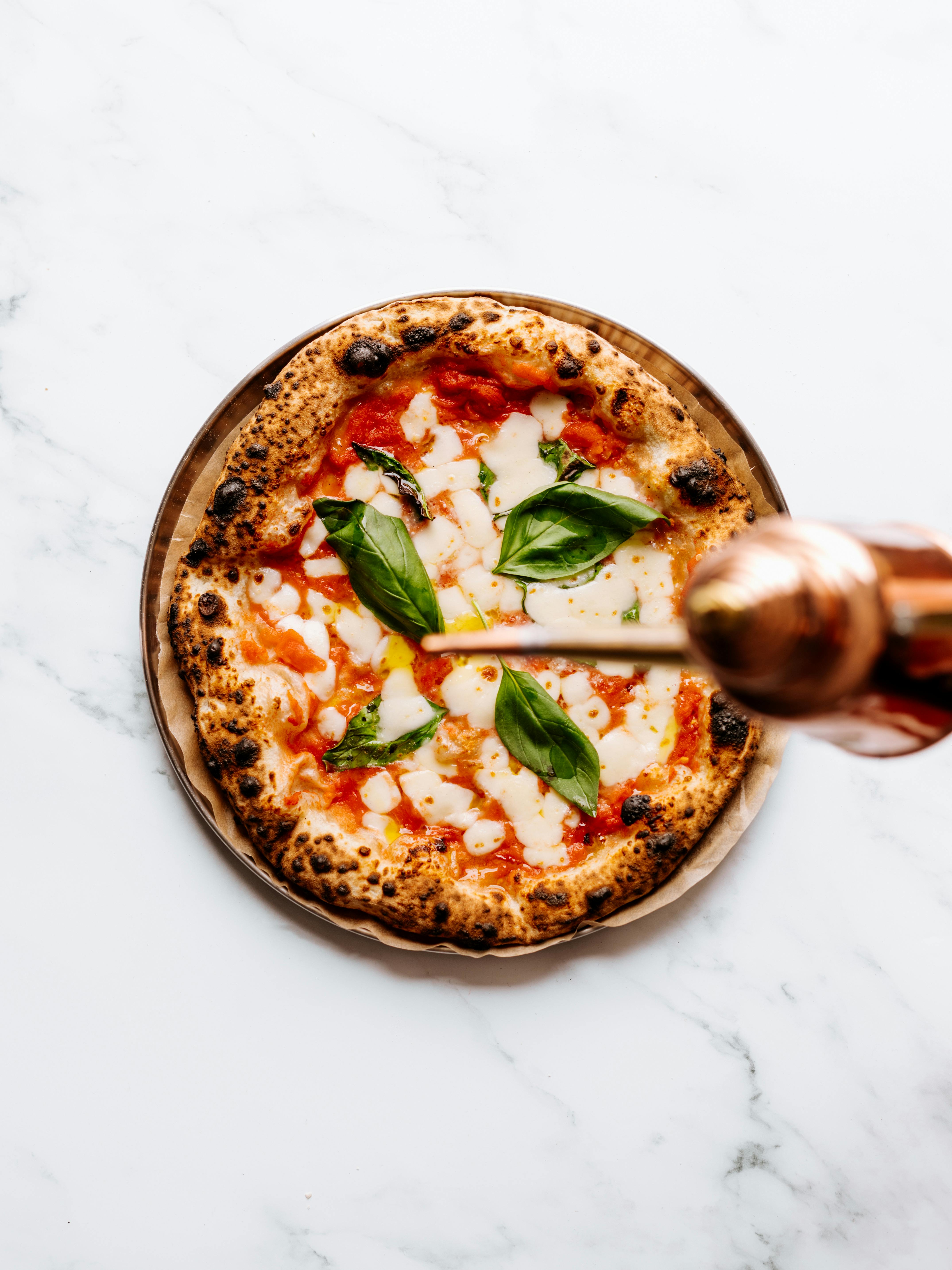 Top view of a margherita pizza on marble, garnished with fresh basil leaves.