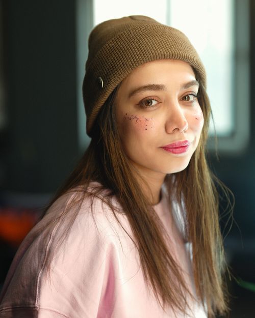 Free Portrait of a young woman with a beanie and subtle makeup, smiling indoors. Stock Photo