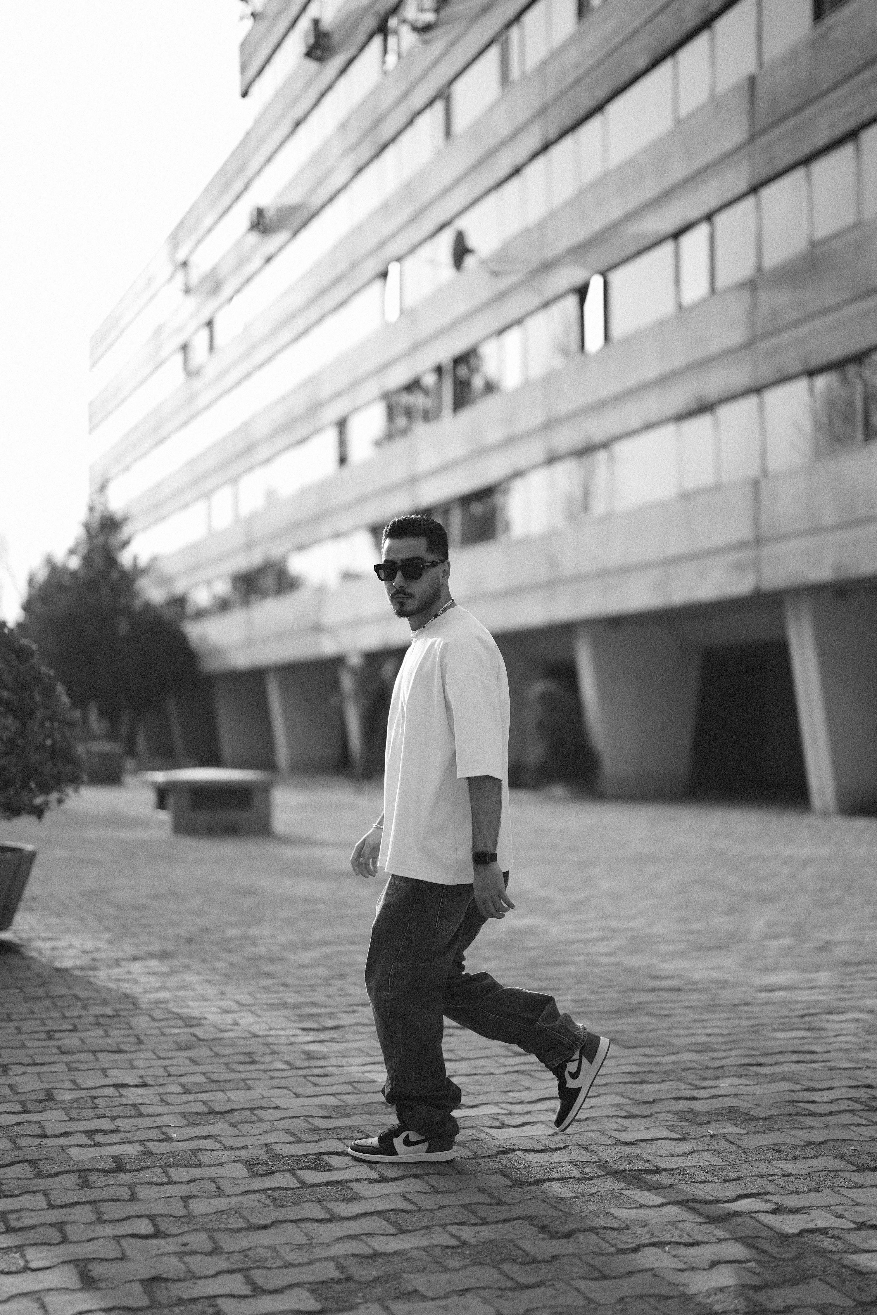 Black and white photo of a man in casual attire walking by a modern building.