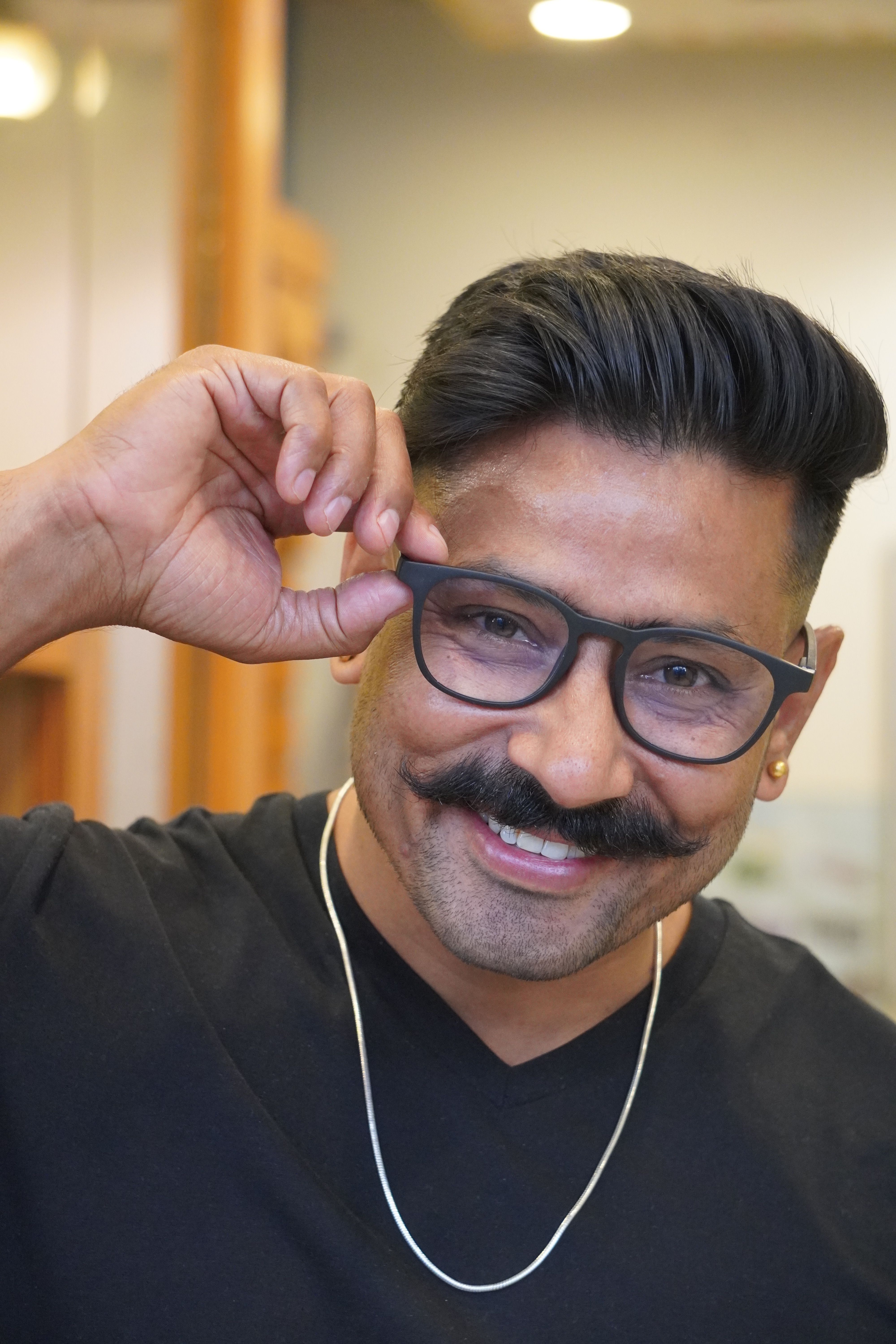 Portrait of a cheerful man adjusting his glasses, radiating confidence and style.