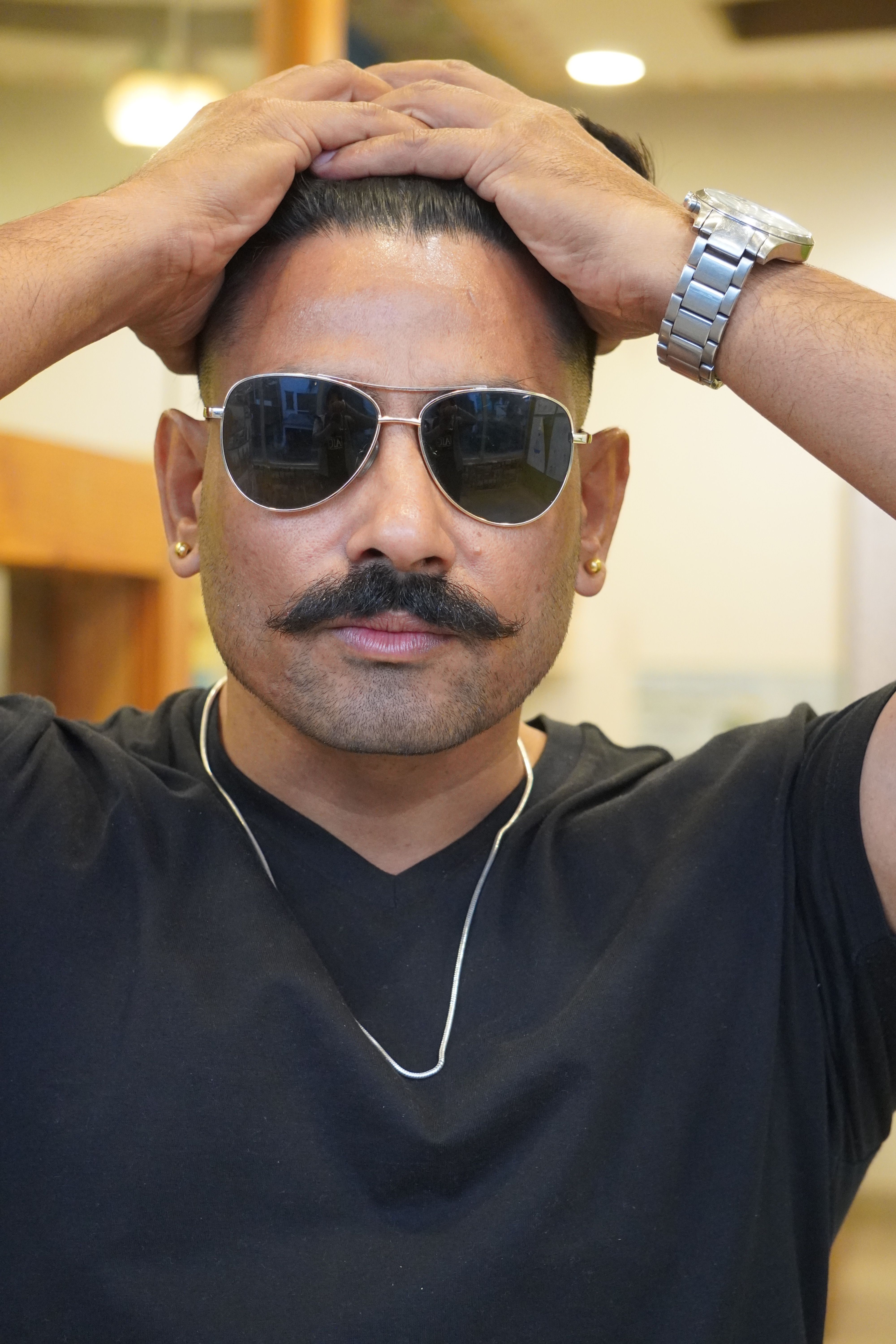 Confident man wearing sunglasses and black outfit indoors.
