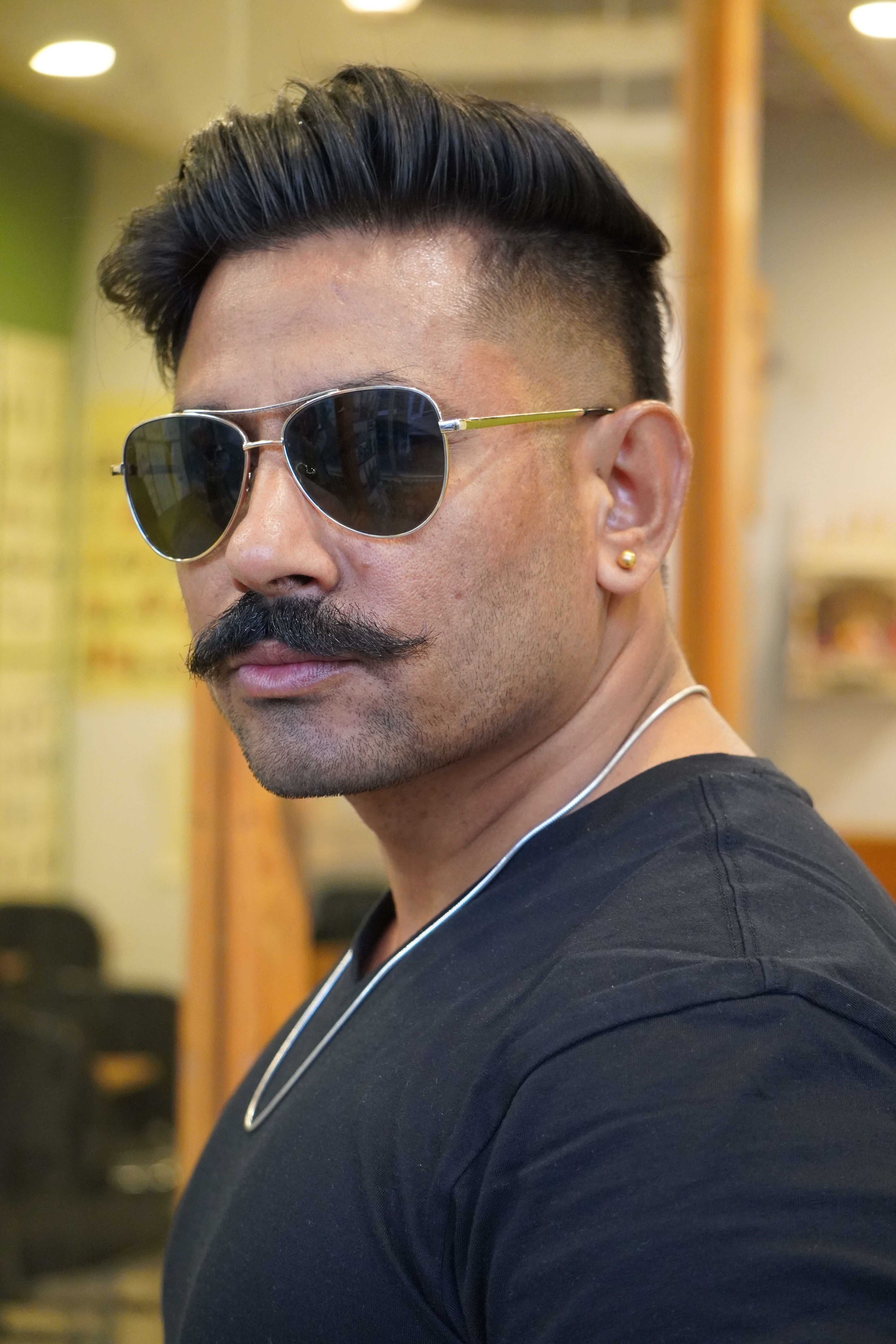 Portrait of a confident man wearing sunglasses and a mustache indoors with stylish accessories.