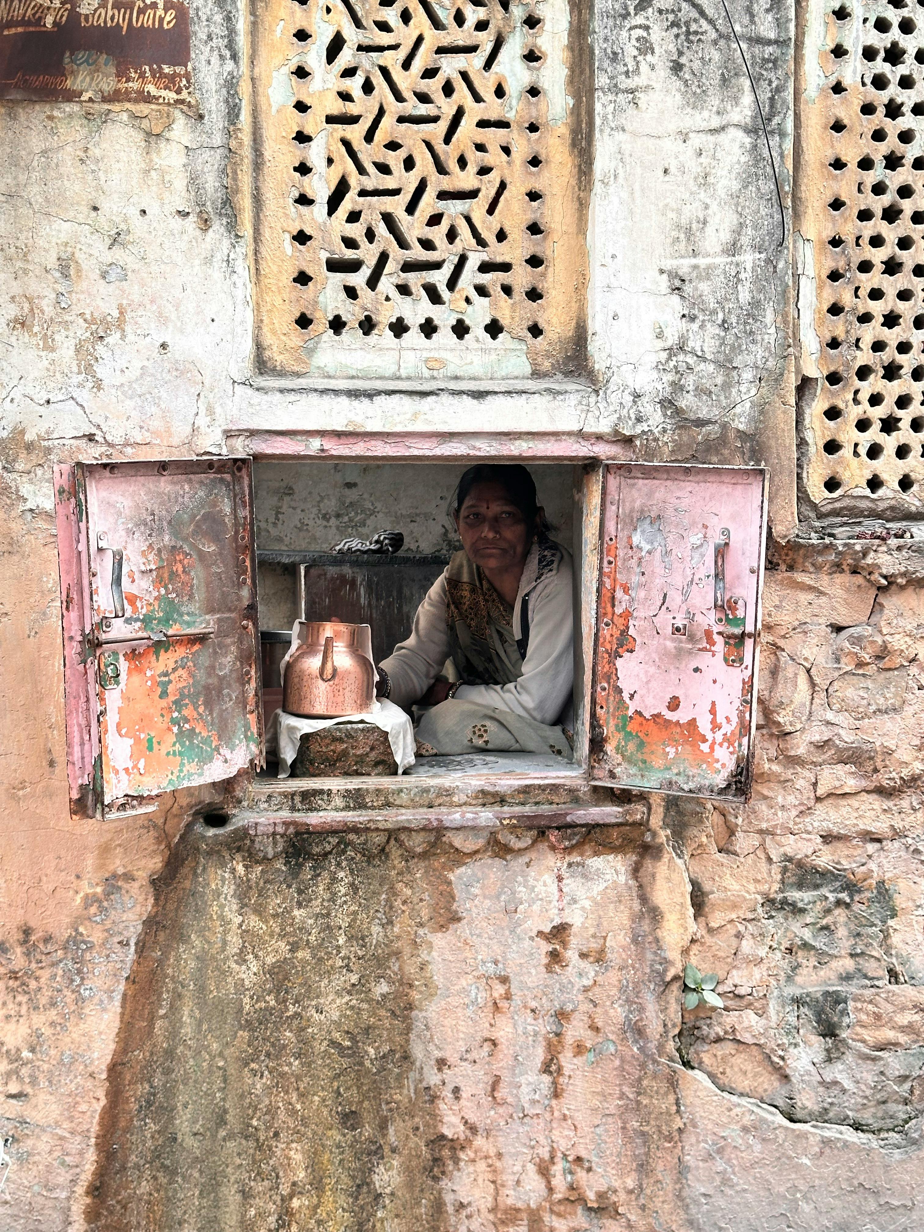 Indian woman in rustic window selling goods in vibrant street setting.