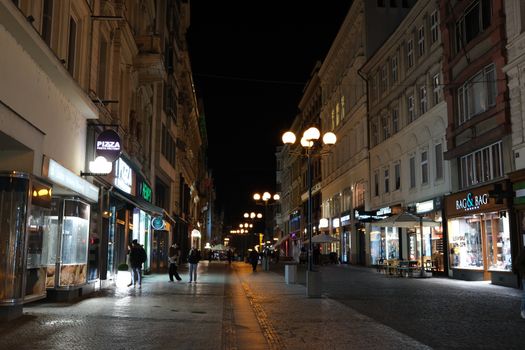 Explore the charming night scene of Prague's streets with glowing lights and vibrant city life.
