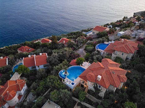 Stunning aerial view of coastal villas with pools and red tiled roofs overlooking the sea.