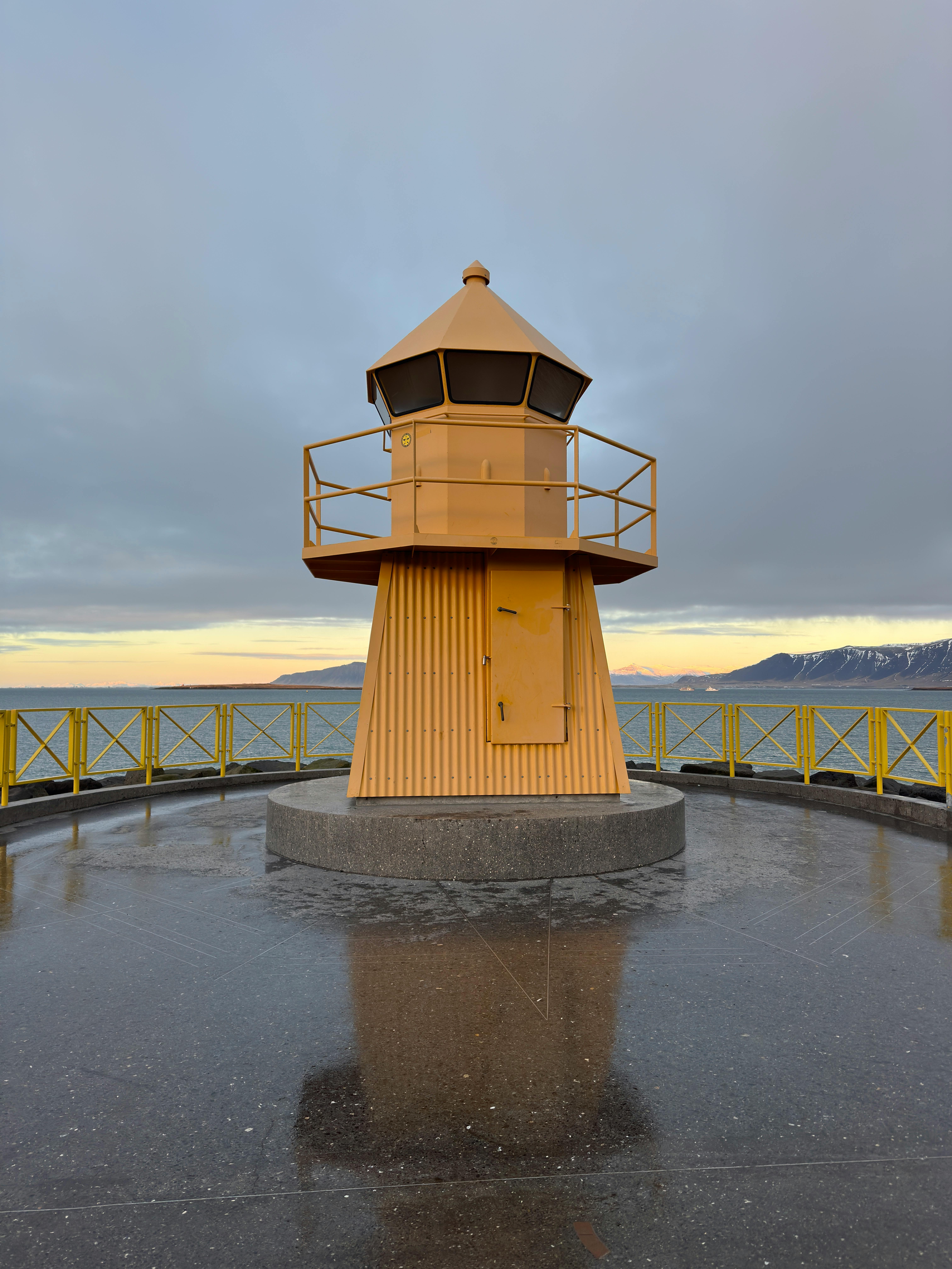 Yellow lighthouse with mountains and sea in Iceland's coastal landscape.