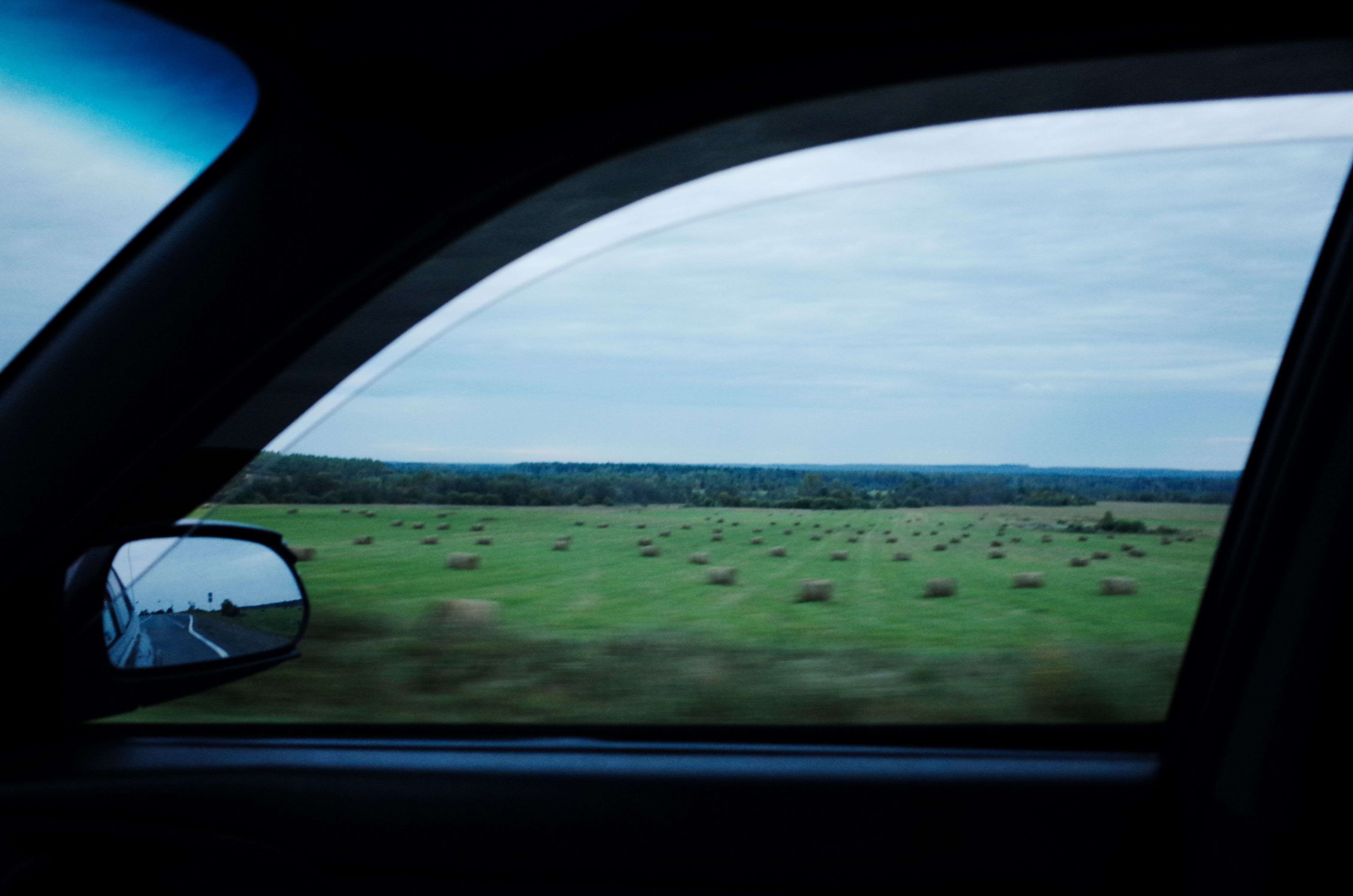 A scenic drive with hay bales on the field captured through a car window during an evening journey.